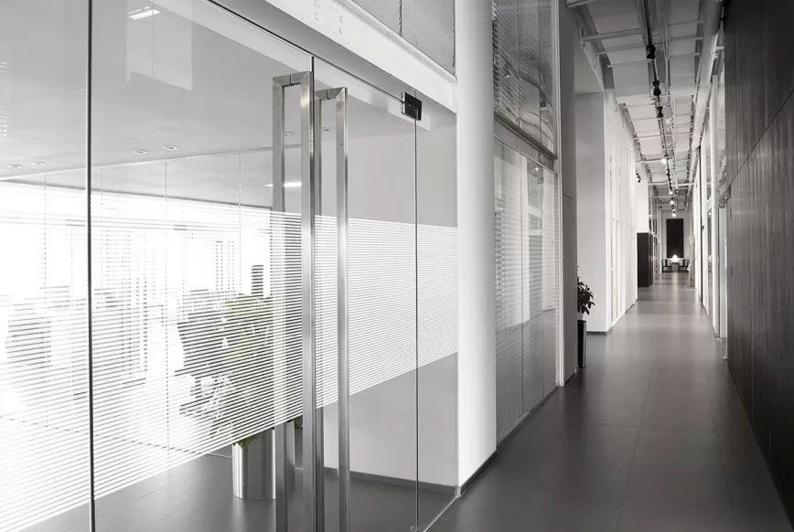 Cloisons vitrées de bureaux habillées d'un film à fines lignes horizontales dépolies, vues depuis un couloir