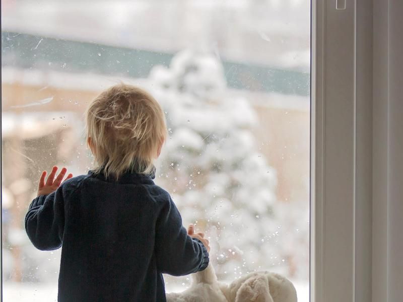 Jeune enfant devant une fenêtre en hiver, jardin enneigé derrière la vitre