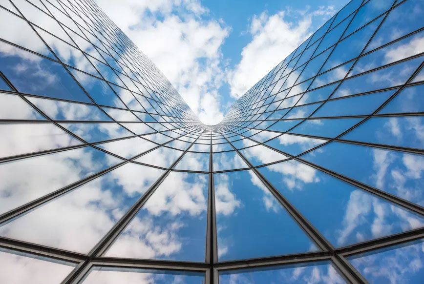 Façade entièrement vitrée d'un immeuble, reflétant le ciel et les nuages
