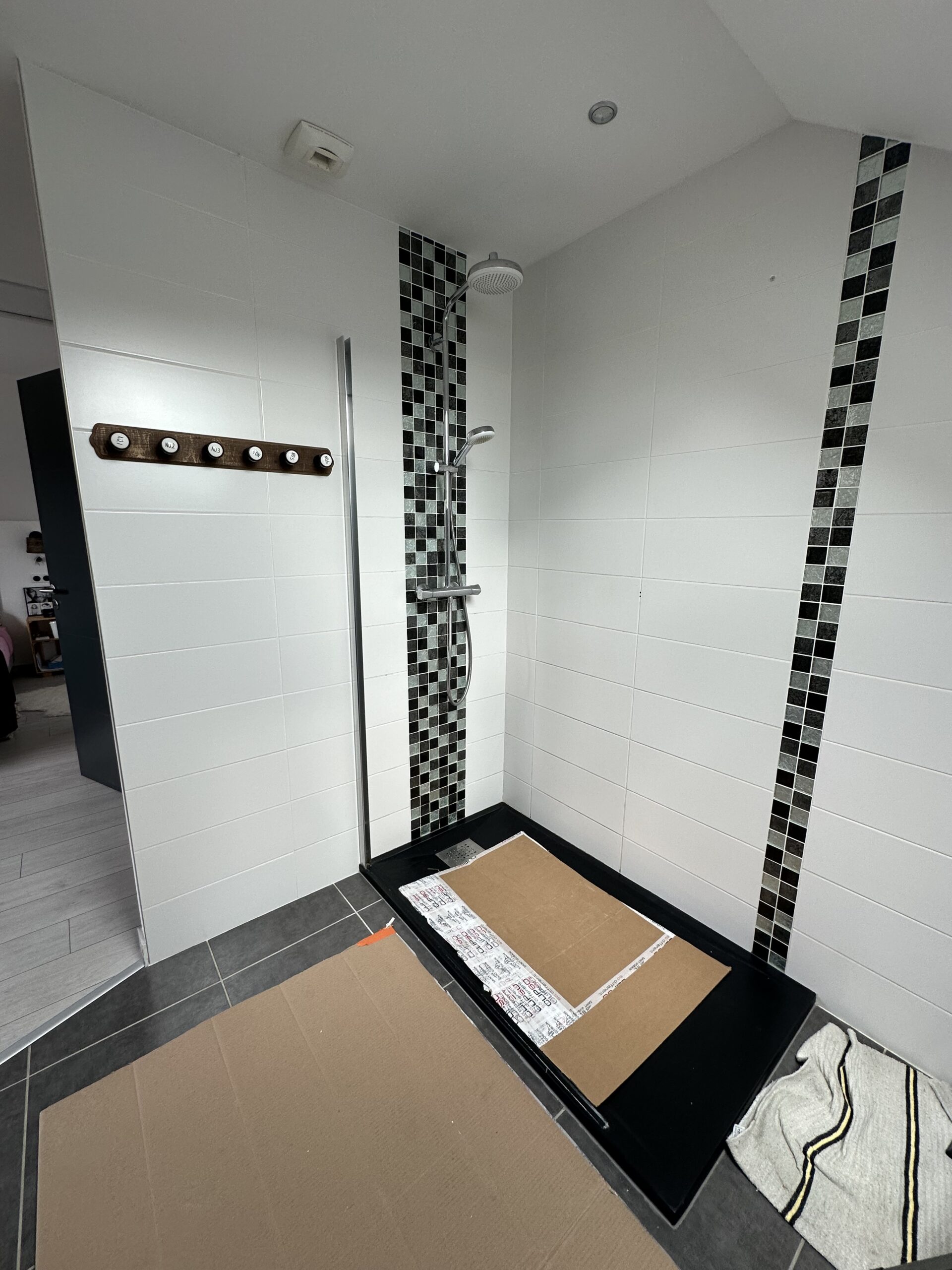 Douche à l'italienne avant rénovation : carrelage blanc et deux bandes verticales de mosaïque noire et grise