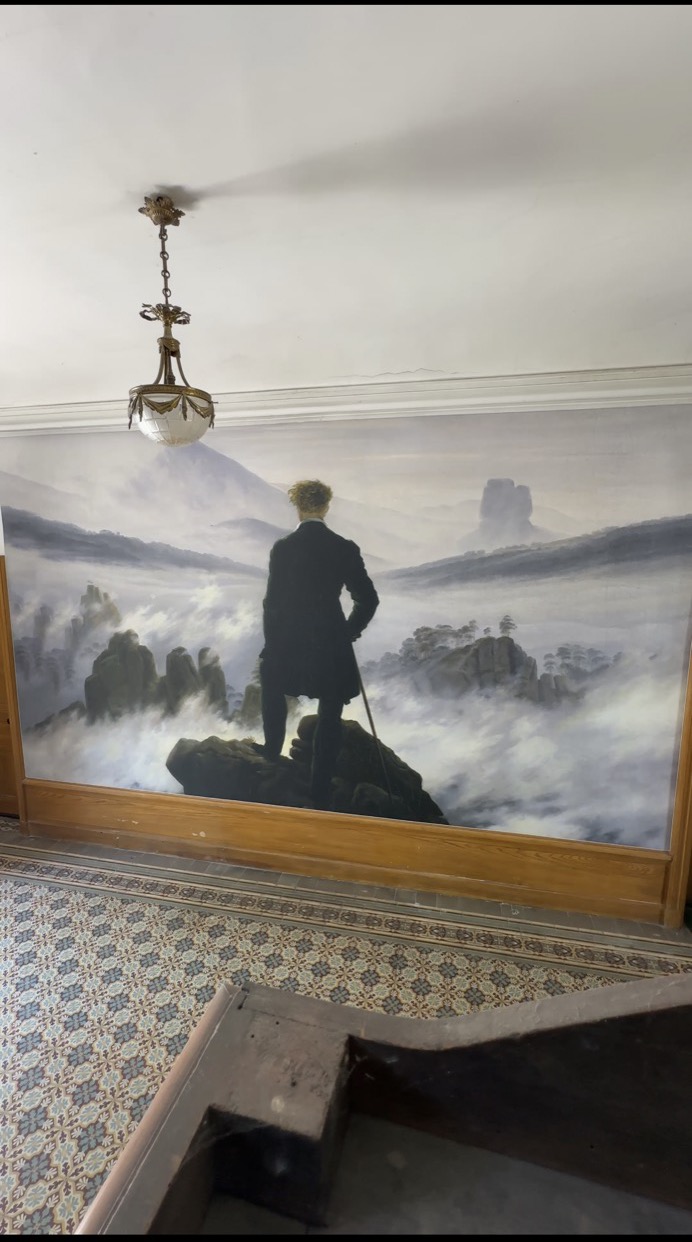 Le même mur recouvert d’une toile tendue imprimée reproduisant Le Voyageur contemplant une mer de nuages de Caspar David Friedrich, bordée d’un cadre en bois clair