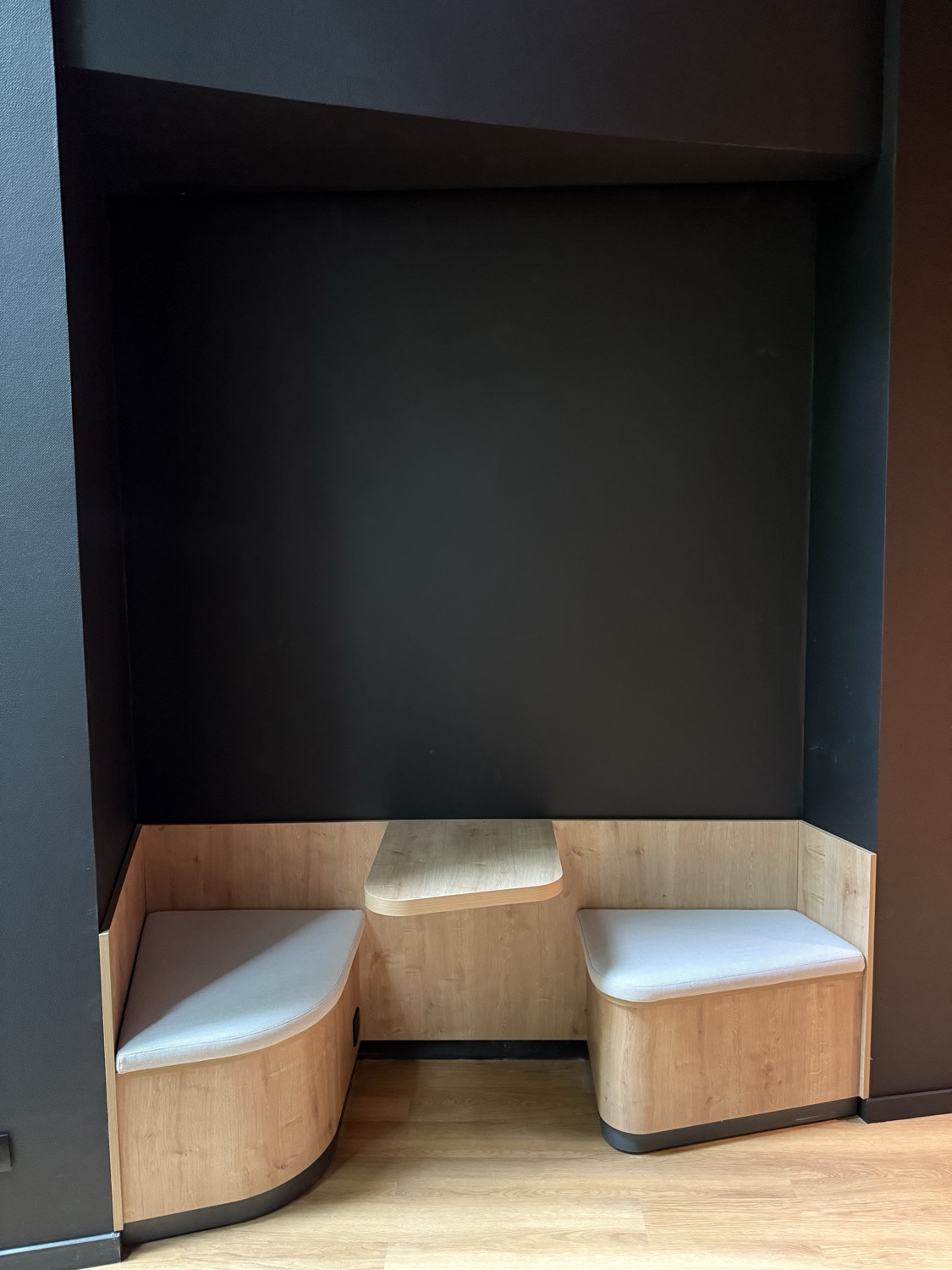 Alcôve de salle d’attente avant intervention : parois noires mates et banquettes en bois clair