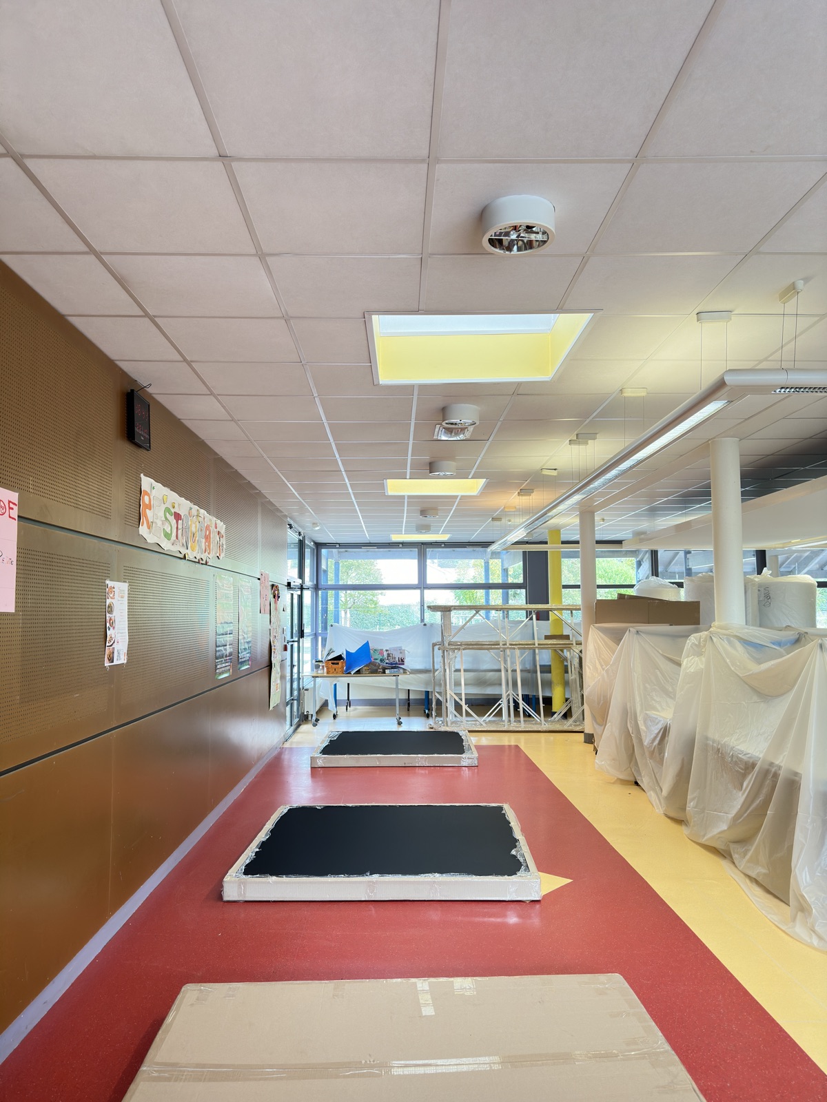 Réfectoire d’école avec le mobilier sous bâche et des cadres acoustiques posés à plat sur le sol avant leur pose